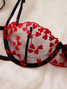 Détail du soutien-gorge en résille noire avec broderie cœur rouge et petit nœud délicat