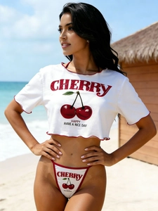 Detail of white crop top featuring red cherry print and cherry text in a beach setting