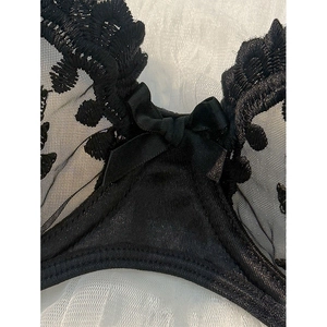 Macro detail of intricate black floral lace and satin bow on the sheer mesh bra cup