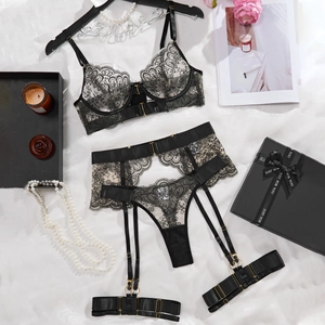Close-up of black floral lace lingerie set with garters on white satin fabric