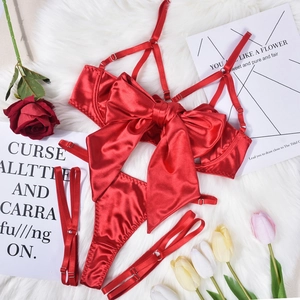 Three-piece red satin lingerie set with large bow detail and tassels on white faux fur background