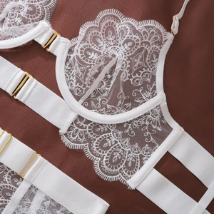 Detail of white floral lace lingerie set with gold metal buckles on a dark background