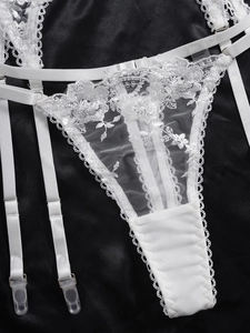 Detailed view of floral embroidery on white lace thong and garter with metal clips