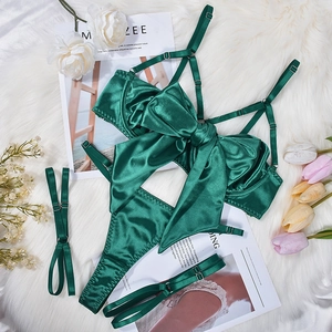 Dark green satin lingerie set with large bow and lace-up leg straps on white plush