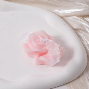 Detailed view of a pink rose scented candle with a ribbon on a white tray
