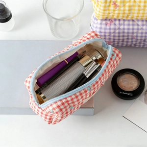 Red plaid quilted makeup bag with blue bow embroidery and zipper closure shown with brushes