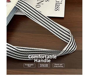 Detail of a beige canvas tote bag featuring black and white striped webbing handles