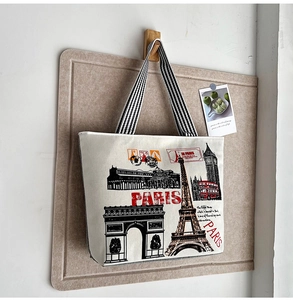 Detail of canvas tote bag with Eiffel Tower print and striped handles on a wooden hook