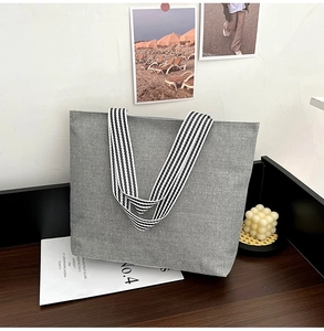 Close-up of grey canvas tote bag with black and white striped straps on wooden table