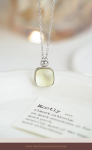 Macro shot of cushion-cut citrine pendant with silver chain over a white plate