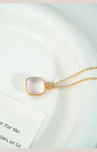 Close-up of a pink square crystal pendant on a gold necklace over a white ceramic tray