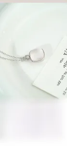 Close-up of S925 silver necklace with square pink crystal pendant in a white ceramic dish