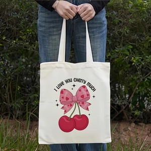 Close-up of a white canvas tote bag with cherry illustration worn on the shoulder outdoors