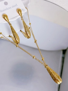 Detailed macro of gold-plated stainless steel jewelry set with textured teardrop pendants
