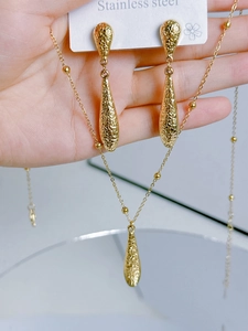 Detail of gold stainless steel necklace and teardrop earrings with hammered texture