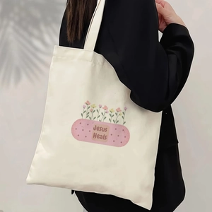 Detail of canvas tote bag with 'Jesus Heals' print worn over the shoulder by model