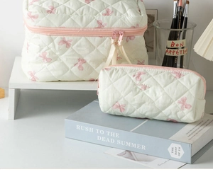 Close-up of quilted cream makeup bag set with light pink bow patterns and zipper detail