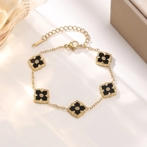 Detail of gold-plated bracelet featuring black clover charms and beaded texture