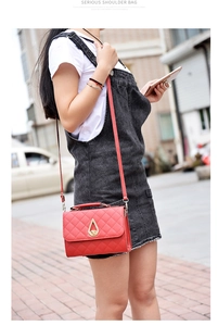 Outdoor shot of a red quilted shoulder bag with a gold water-drop clasp on a denim outfit