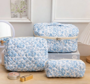 Three-piece floral quilted cotton cosmetic bag set on a wooden table with elegant decor