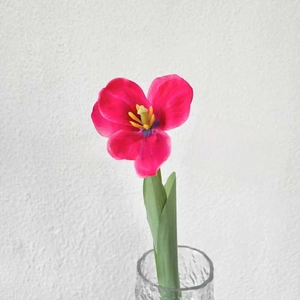 Close-up of vibrant magenta artificial tulip with yellow pistil in embossed glass vase
