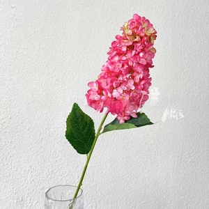 Close-up of vibrant magenta artificial hydrangea with green leaves in a glass vase