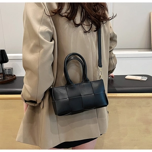 Dettaglio della borsa in pelle intrecciata nera con fibbie dorate su un abito beige