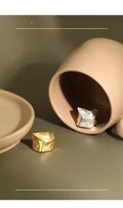 Macro detail of minimalist gold and silver rings with irregular rock texture on a ceramic plate
