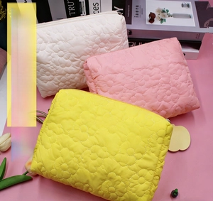 Detailed view of quilted flower makeup bags in cream, pink, and yellow with floral tags