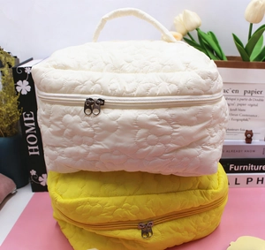 Close-up of quilted floral cosmetic bags with dual zippers and handle in ivory and yellow