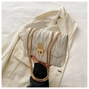 Detail of white matelasse shoulder bag showing gold chain and turn-lock closure