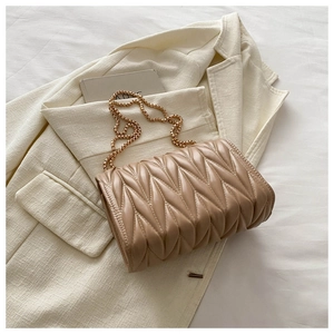 Close-up of beige matelassé quilted bag with gold chain strap on a white blazer