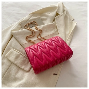 Detail of rose red quilted crossbody bag with gold ball chain on white blazer