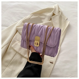 Close-up of light purple quilted shoulder bag with gold chain and rectangular metal twist lock