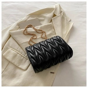 Close-up of black matelassé quilted handbag with gold chain strap on a white blazer