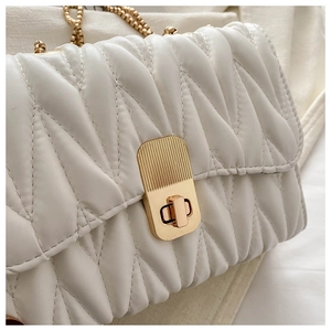 Close-up of quilted white leather bag featuring a gold buckle and luxury chain strap
