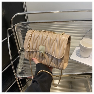 Close-up of beige quilted crossbody bag with wavy texture and golden chain strap