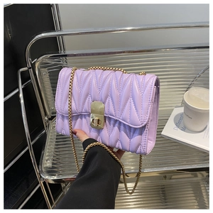 Detail of lavender quilted square bag with gold twist lock and metal chain on a chair