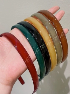 Détail de six serre-têtes en résine colorée tenus à la main avec une finition brillante