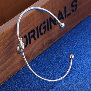 Minimalist silver knot cuff bracelet with ball ends displayed on a vintage wood background