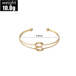 Close-up of golden knotted open cuff bracelet with metal beads and polished finish