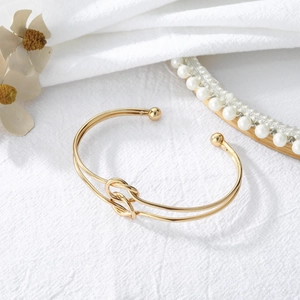 Close-up of a gold knotted open bangle with metal spheres on a textured fabric