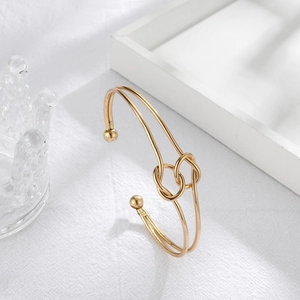 Detail of gold-plated knot bracelet featuring double interlocking knots and ball-end caps