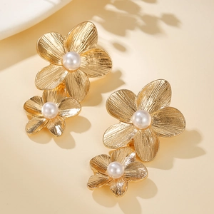 Detailed close-up of golden floral pearl earrings with brushed texture on warm beige background
