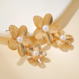 Detailed view of golden flower earrings with brushed metal texture and white pearls