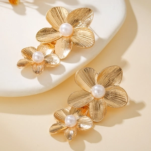 Detail of gold flower earrings with brushed metal texture and central white pearls