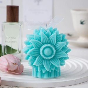 Detailed view of sunflower candle in blue on white pedestal with decorative floral setting
