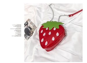 Detail of red strawberry crossbody bag with glossy finish and silver chain strap