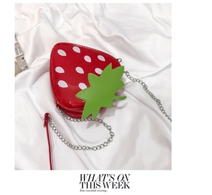 Detailed view of strawberry shaped crossbody bag with red glossy finish and green leaf detail