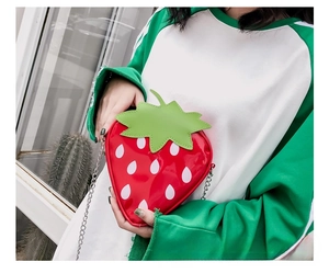 Close-up of a creative strawberry-shaped crossbody bag with a shiny red finish and silver chain